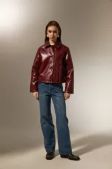 Chaqueta de eco-cuero negro con acabado brillante, cuello camisero, cierre frontal con botones y mangas largas.