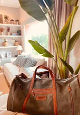 Bolso de viaje verde de cuero vacuno, con detalles en cuero marrón. Tiene doble asa de mano y correa desmontable para el hombro, cierre superior con cremallera, bolsillos exteriores e interiores.