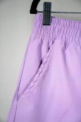 Short deportivo lila con cintura elástica, bolsillos laterales y logo estampado en azul en la pierna izquierda.