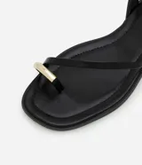 Sandalias planas negras con tira fina en el dedo y pulsera al tobillo con hebilla y aplique dorado.