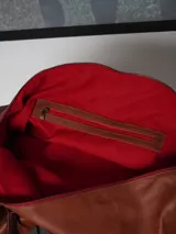 Bolso de viaje tipo weekender de cuero color tostado con asas y detalles en marrón oscuro, herrajes metálicos y bolsillo frontal con cierre.