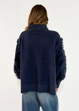 Sweater de punto color azul marino con cuello alto, diseño de rombos en relieve y detalles de flecos en las costuras de las mangas. Presenta un corte holgado con aberturas laterales en el ruedo.