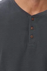 Remera de algodón texturada color gris oscuro, de manga larga, con cuello redondo y botones en la parte frontal. Presenta un pequeño logo bordado en el pecho y un parche decorativo en la manga izquierda.