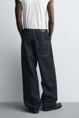 Jeans de denim oscuro, corte ancho (baggy fit) y tiro medio, con costura central girada en el frente de ambas piernas. Presenta pespuntes en color caramelo.