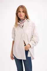 Camisa de corte oversize con estampado de rayas verticales finas en color azul sobre fondo claro. Presenta cuello clásico, cierre frontal con botones y un bolsillo aplicado en el pecho.