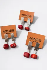Aros colgantes compuestos por una pieza rectangular metálica plateada y un dije inferior de piedra roja resinosa con detalle cúbico metálico.