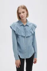Camisa celeste de jean con cuello clásico, cierre frontal con botones y volados en el canesú delantero y trasero.