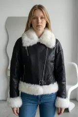 Campera tipo gamulán de ecocuero negro con interior y detalles de piel sintética blanca en cuello, puños y ruedo. Presenta cierre frontal, cinturón ajustable en la cintura y bolsillo con cierre en la manga.