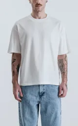 Remera de corte holgado y diseño minimalista, con cuello redondo y mangas cortas de hombros caídos. Confeccionada en algodón premium, presenta un largo a la altura de la cadera.