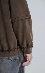 Buzo de cuello redondo color marrón oscuro con efecto desgastado (lavado óxido). Presenta costuras expuestas y detalles de pespunte ondulado en puños y ruedo. Tiene un calce oversize y crop.