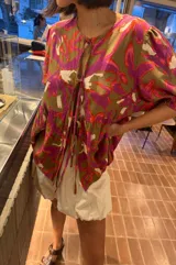 Blusa de calce holgado con estampado floral en tonos marrones, fucsias, naranjas y blancos. Tiene escote en V con doble lazo ajustable y mangas 3/4 con volumen.