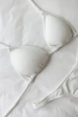 Bikini blanco de lycra texturizada, compuesto por un corpiño de triángulos movibles con tiras finas para atar al cuello y espalda, con almohadillas desmontables, y una bombacha colaless con laterales fijos.