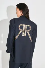Saco sastrero de corte oversize, color negro, con cierre frontal de botones, bolsillos delanteros y forro interior de tafeta. Presenta una estampa grande en la espalda con las letras RR en diseño animal print.