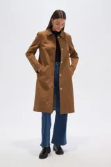 Abrigo tipo gabardina o trinchera de largo medio, color camel, con cuello camisero y cierre frontal de botones dorados. Presenta un corte recto y holgado.