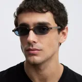 Lentes de sol con montura ovalada de color gris translúcido y cristales color celeste. Presentan un diseño estilizado y ligero con protección UV400.