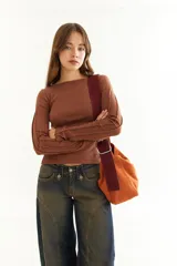 Top de manga larga color marrón, confeccionado en tejido acanalado con cuello bote. Presenta costuras decorativas expuestas a lo largo de las mangas, creando un efecto de relieve.