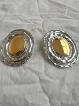 Par de aros grandes ovalados con centro dorado y borde plateado texturizado.