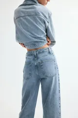 Jean tobillero de denim de algodón rígido, de tiro alto y diseño curvo con volumen en las piernas. Presenta cinco bolsillos, cierre de cremallera y botón, pinzas en las rodillas y costuras laterales avanzadas.