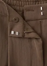 Pantalón de corte recto y tiro regular, color marrón, con bolsillos laterales y traseros con ribete. Cierre frontal con cremallera, botón y ganchos ocultos.