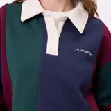 Buzo estilo rugby de la marca Rusty, con diseño color block en tonos bordó, verde y azul marino. Presenta cuello polo en color crema con cierre frontal de botones, mangas largas con puños elásticos y logo bordado en el pecho.