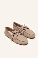 Mocasín estilo náutico de gamuza marrón, con cordones de cuero, borla decorativa y cuentas de colores en el empeine.