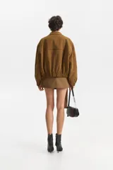 Chaqueta estilo bomber de color marrón, confeccionada en una mezcla de algodón y poliéster. Presenta cuello tipo camisa, cierre frontal y elástico en el bajo.