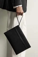 Bolso tipo sobre negro con acabado texturizado y detalle de banda horizontal lisa. Cuenta con compartimento principal con cierre de cremallera, bolsillo frontal plano, asa de mano corta y organizador interno para tarjetas.