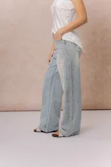 Jean wide leg tiro alto de lavado claro, con diseño de cinco bolsillos, cierre frontal con botón y aplicación de strass en degradé a lo largo de los laterales.
