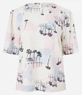 Blusa de viscolino color crudo con estampado de paisaje con palmeras y casas en tonos pastel. Tiene cuello redondo y mangas cortas abullonadas.