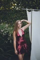 Vestido corto negro con escote en V profundo, estilo halter con tiras para atar al cuello. Presenta un diseño ajustado en el busto con tiras ajustables bajo el mismo que se cruzan y anudan en la espalda, y falda con volado en el ruedo con detalle de encaje.