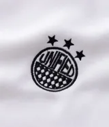 Buzo deportivo de felpa en color blanco con detalles en negro. Presenta cuello tipo polo, mangas largas con puños acanalados y diseño con recortes laterales. Incluye estampados gráficos en el frente con tipografía cursiva y emblema circular.