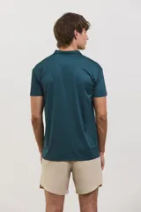 Chomba deportiva de manga corta, color verde oscuro, con cuello polo y cierre frontal de dos botones. Presenta un diseño entallado con tejido técnico transpirable y elástico, ideal para actividades deportivas.