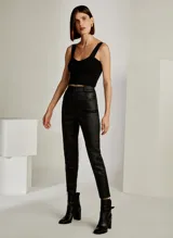 Pantalón de cuero negro, corte skinny, tiro alto, con cierre de botón y cremallera, bolsillos delanteros y acabado cosido.