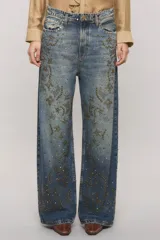 Jeans de tiro medio y calce holgado, color azul con lavado desgastado. Presenta tachas metálicas aplicadas en la parte frontal formando patrones decorativos y en la pretina.