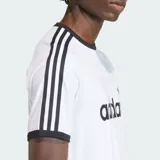 Remera Adidas modelo 3S Ringer de color blanco, con cuello redondo y ribetes en las mangas de color negro. Presenta el logotipo y el texto de la marca estampados en el pecho en color negro, junto con las clásicas tres tiras en los hombros y mangas.