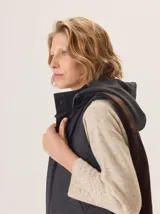 Chaleco con capucha, presenta una espalda de pelo sintético en color marrón oscuro con etiqueta de cuero negra y una capucha de tela tipo denim azul. Diseño original con mezcla de texturas.