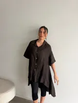 Camisola de lino color beige, de corte amplio, con cierre frontal de botones y diseño asimétrico más largo en la parte trasera.