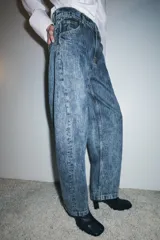 Jeans de tiro alto, estilo balloon leg, largo completo. Denim azul claro con efecto lavado ácido o 'acid wash'. Presenta cinco bolsillos y cierre frontal con cremallera y botón.
