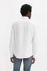 Camisa de lino blanca con cuello clásico, cierre frontal de botones, manga larga y un bolsillo aplicado en el pecho con etiqueta roja de la marca.