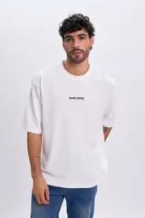 Remera blanca de manga corta y corte oversize, con estampa en la espalda en tono bordó con nombres de ciudades y texto "International vibes from the retro streets".