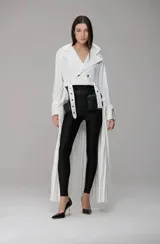 Mono largo de diseño minimalista con cuerpo superior tipo blazer cruzado de color blanco y parte inferior tipo calza ajustada de color negro. Presenta un cinturón integrado con mini bolsos tipo cartuchera y una falda plisada superpuesta en la parte trasera.