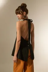 Chaleco largo negro, con escote halter y abertura frontal con botones joya. Corte entallado en la parte superior y ligeramente acampanado en el bajo.