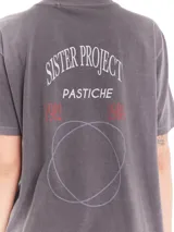 Remera de cuello redondo y manga corta con calce oversized, confeccionada en algodón lavado con efecto desgastado. Presenta estampa gráfica en la espalda con el texto 'Sister Project Pastiche' y diseño de círculos entrelazados.