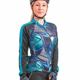 Remera de ciclismo de poliéster con cierre frontal completo, mangas largas con puños elásticos y tres bolsillos traseros. Diseño con estampado geométrico en tonos azul, celeste, violeta y blanco, con detalles en negro y turquesa.