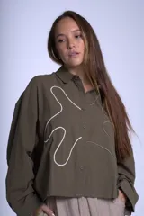 Camisa negra de manga larga con cuello clásico y cierre frontal con botones. Presenta bordados abstractos en blanco y negro en el frente.