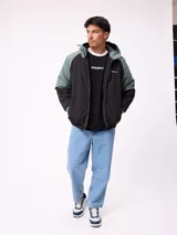 Campera Rusty con capucha, diseño bicolor en negro y verde militar. Presenta cierre frontal, puños elásticos y logo de la marca bordado en el pecho.