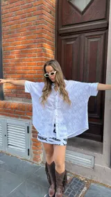 Camisa blanca de broderie con escote en V, abotonada y manga 3/4. Corte oversize, más larga atrás que adelante.