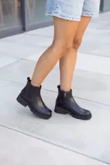 Bota corta estilo Chelsea de cuero negro, con elástico lateral y cierre de cremallera en el talón. Posee suela track gruesa y taco bajo.