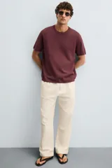 Pantalón de corte recto, color beige claro, con pliegues frontales y bolsillos de vivo en la parte trasera.