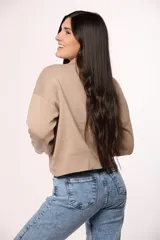 Buzo tejido de punto en color blanco crema, con cuello redondo alto y mangas largas con puños acanalados.